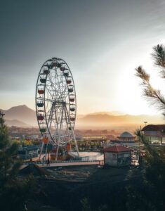 Captivating view of a Ferris wheel in an amusement park at sunset, set against a scenic mountain backdrop.